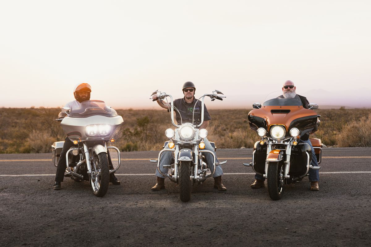 Three motorcycle riders on a scenic road at sunset