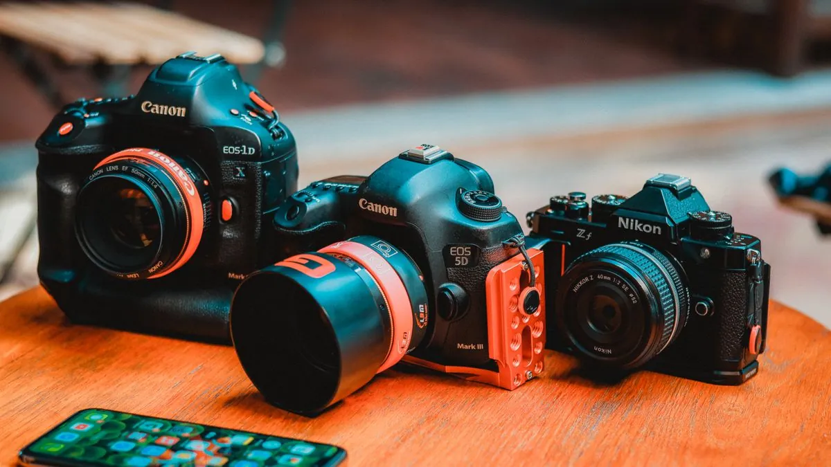 Professional mirrorless cameras on a wooden table representing the Canon R1, Sony A1 II, and Nikon Z6 III flagship comparison